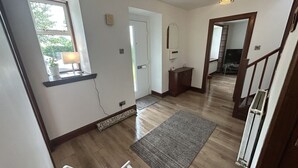 A spacious room with a wooden floor, a white door, a small window with a lamp, and a staircase leading to another level.