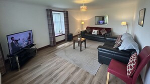 A living room with a flat-screen TV, a sofa, a red armchair, a coffee table, and a window with curtains.