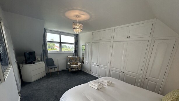 A bedroom with a large bed, a wardrobe, a desk, a chair, and a television.