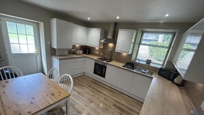 A modern kitchen with white cabinets, a wooden dining table, and a built-in oven.