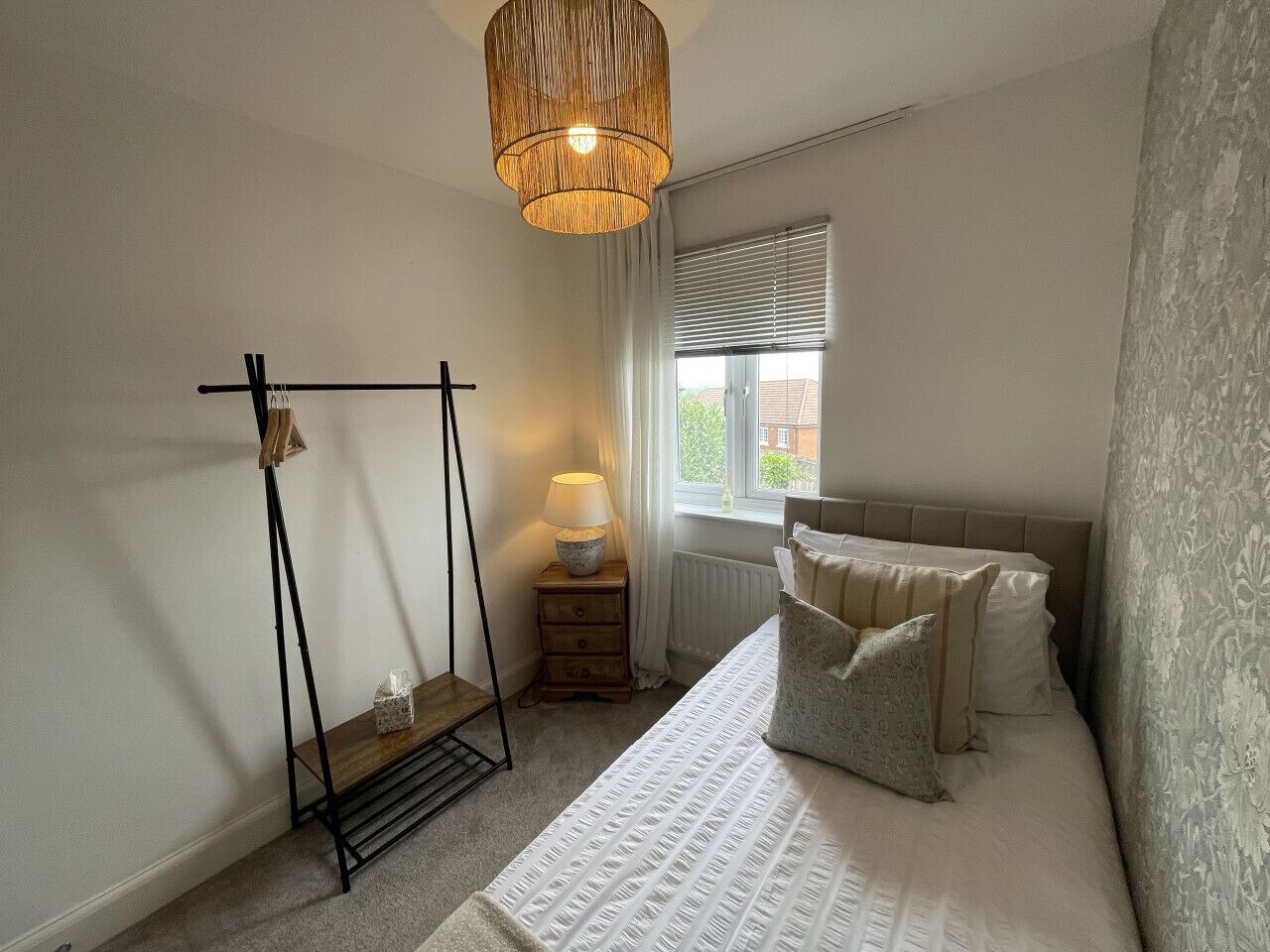 A bedroom with a bed, a hanging chair, a bedside table with a lamp, and a window with blinds.