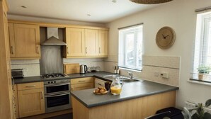 A modern kitchen with wooden cabinets, a gas stove, a built-in oven, and a large island with a sink. - Greenfields House Ashford (Kent)
