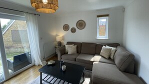 A modern living room with a sectional sofa, a black coffee table, and a large window with curtains. - Greenfields House Ashford (Kent)