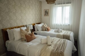 A hotel room with two beds, each with white linens and multiple pillows. There is a large window with sheer curtains, a framed picture on the wall, and a woven headboard. - Greenfields House Ashford (Kent)