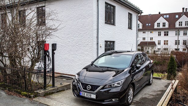 Un coche negro estacionado frente a un edificio blanco, con una patente visible.