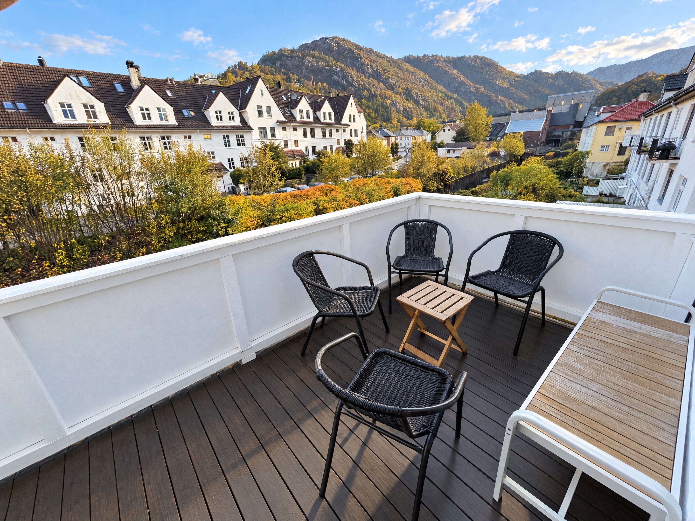 Une terrasse avec quatre chaises et une petite table, d’où l’on peut admirer une ville avec ses maisons et ses montagnes.