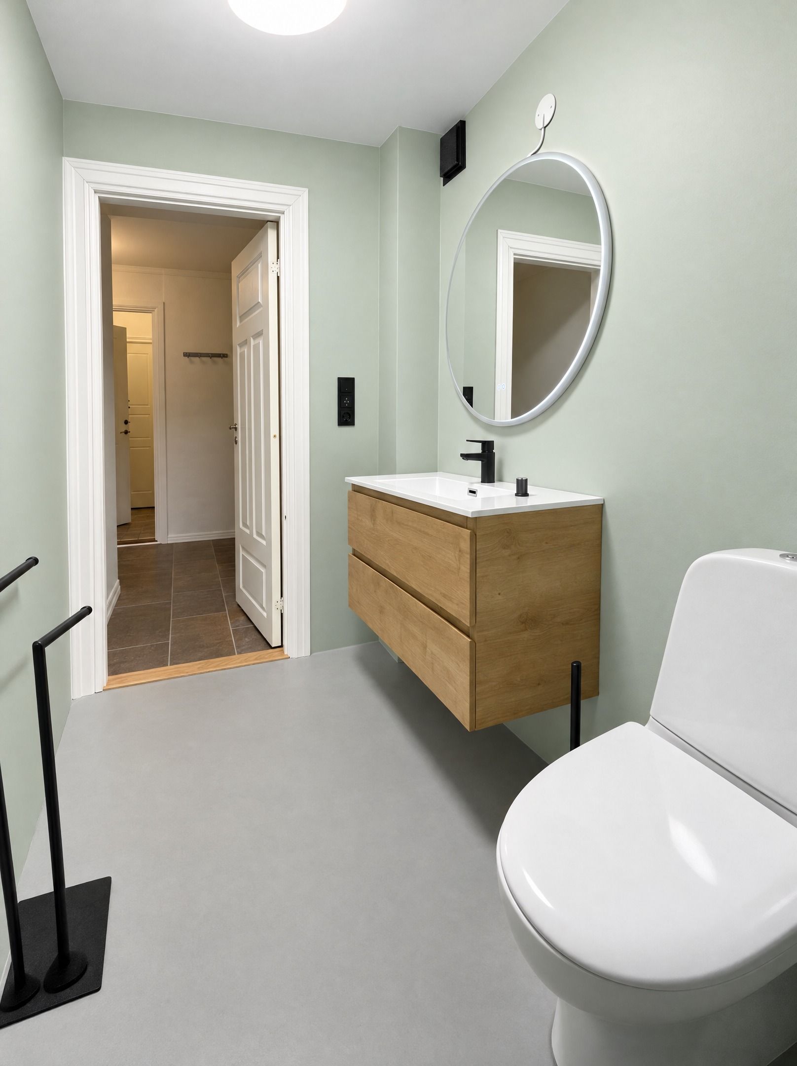 A bathroom with a white toilet, a wooden vanity with a mirror, and a tiled floor.