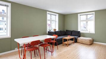 Une pièce avec une table blanche, des chaises rouges, un canapé gris et une petite table en bois.