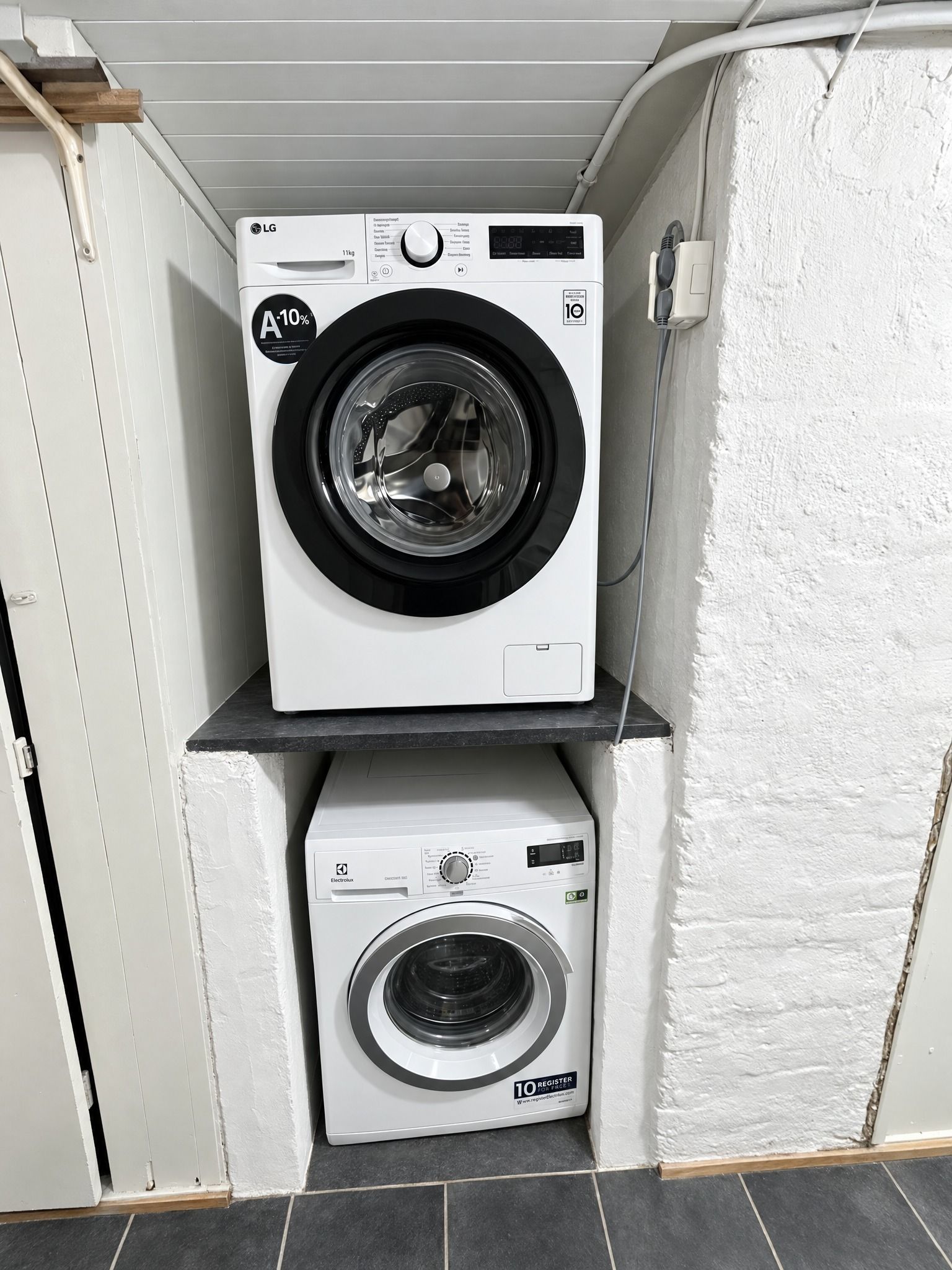 Two stacked washing machines in a corner with a white wall and a wooden door.