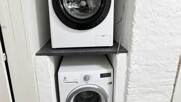 Two stacked washing machines in a corner with a white wall and a wooden door.