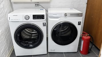 Twee Samsung wasmachines met voorlader en digitale bediening, naast een brandblusser op een betegelde vloer.