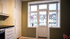 Una cocina con armarios blancos, encimera negra y ventana con vista a casas.