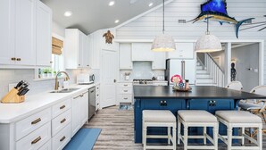 Een moderne keuken met witte kasten, een blauw eiland en hanglampen.