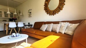 Una sala de estar con un sofá marrón, una mesa de centro blanca y un espejo de madera con diseño de sol en la pared.