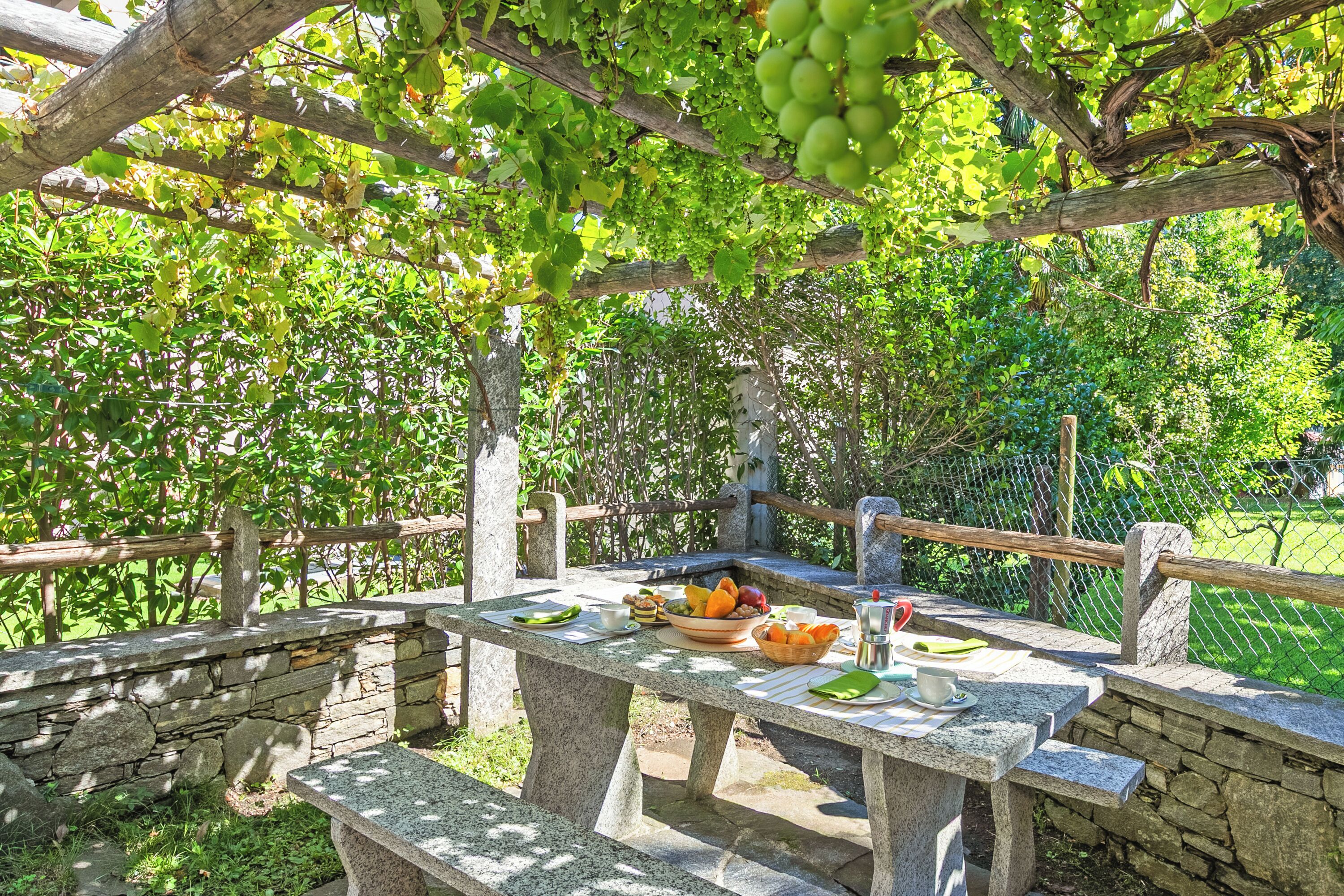 A stone table set outdoors with a basket of fruits and a glass of water.