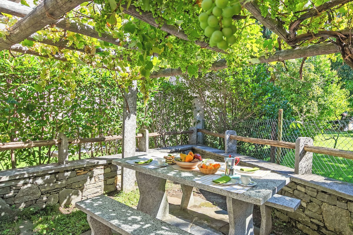 A stone table set outdoors with a basket of fruits and a glass of water.