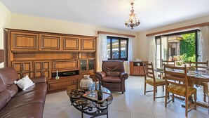 A spacious living room with a brown leather sofa, a wooden cabinet, a dining table with chairs, and a chandelier. - Casa Ana - Losone Center (Losone)