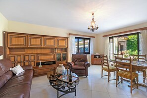 A spacious living room with a brown leather sofa, a wooden cabinet, a dining table with chairs, and a chandelier. - Casa Ana - Losone Center (Losone)