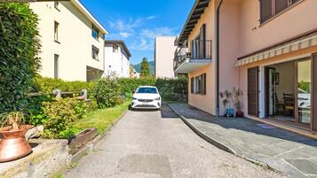 Una calle estrecha con un coche blanco estacionado al costado, bordeada por edificios con balcones y macetas.
