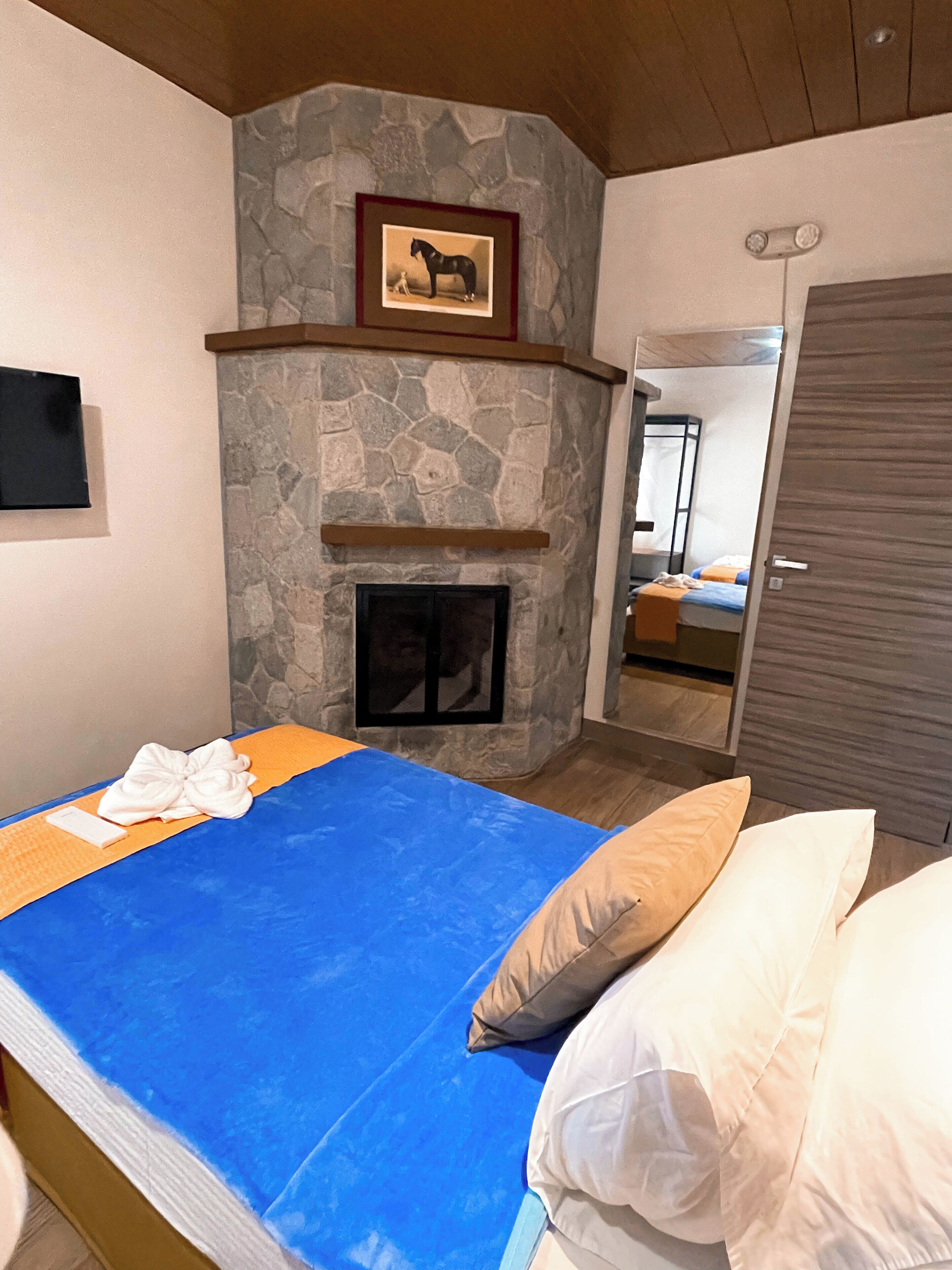Quarto com lareira de pedra, cama com roupa de cama azul e teto de madeira.