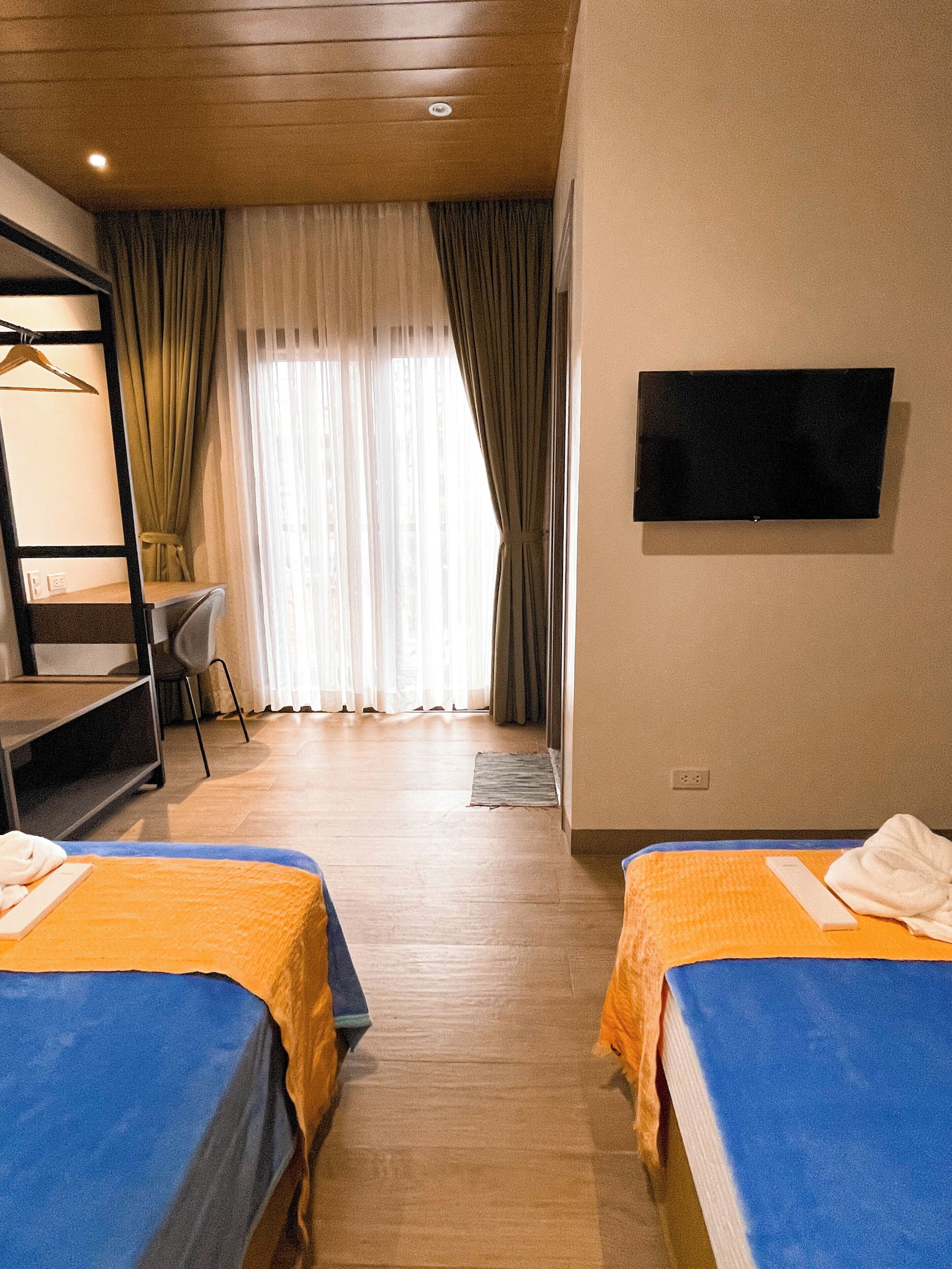 Une chambre d’hôtel avec deux lits, un bureau, une chaise, une télévision et une fenêtre avec des rideaux.