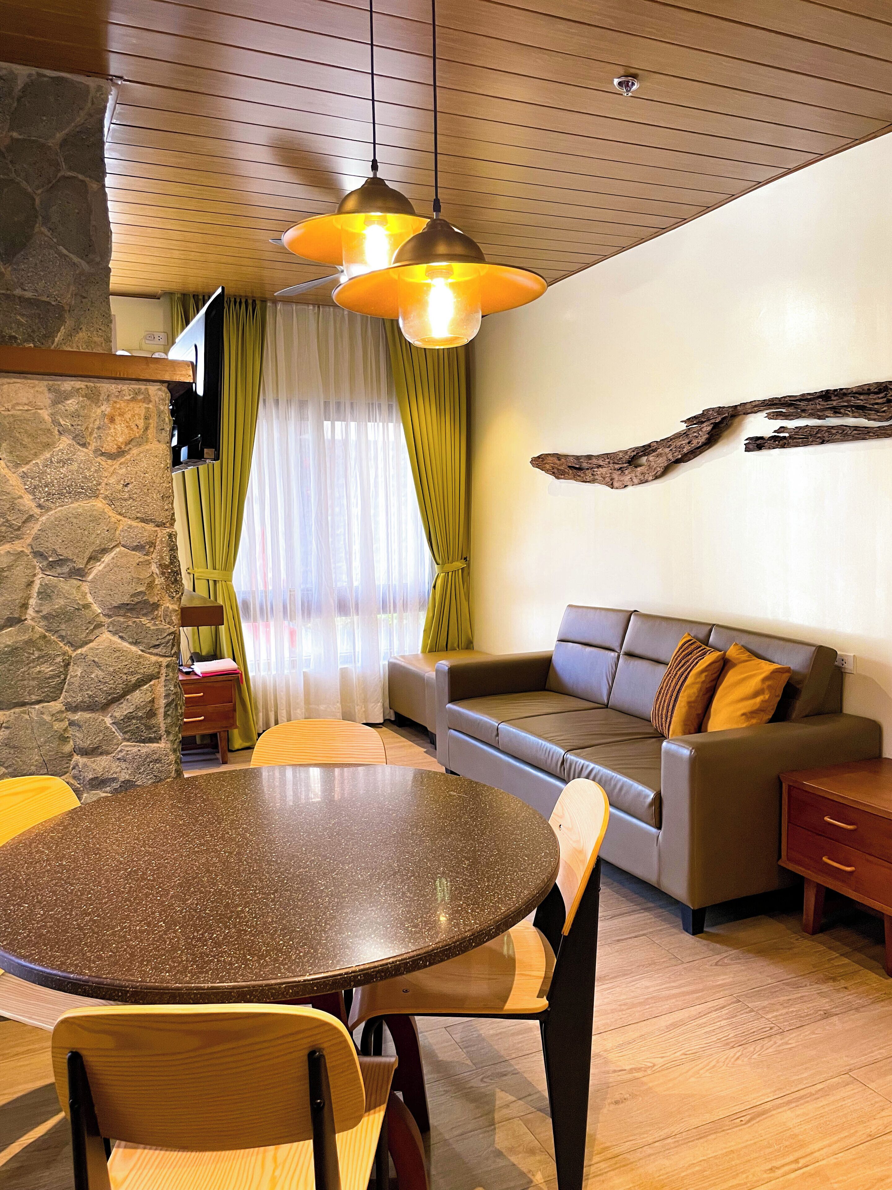 A modern living room with a stone accent wall, a round dining table, a sofa, and a wooden ceiling.