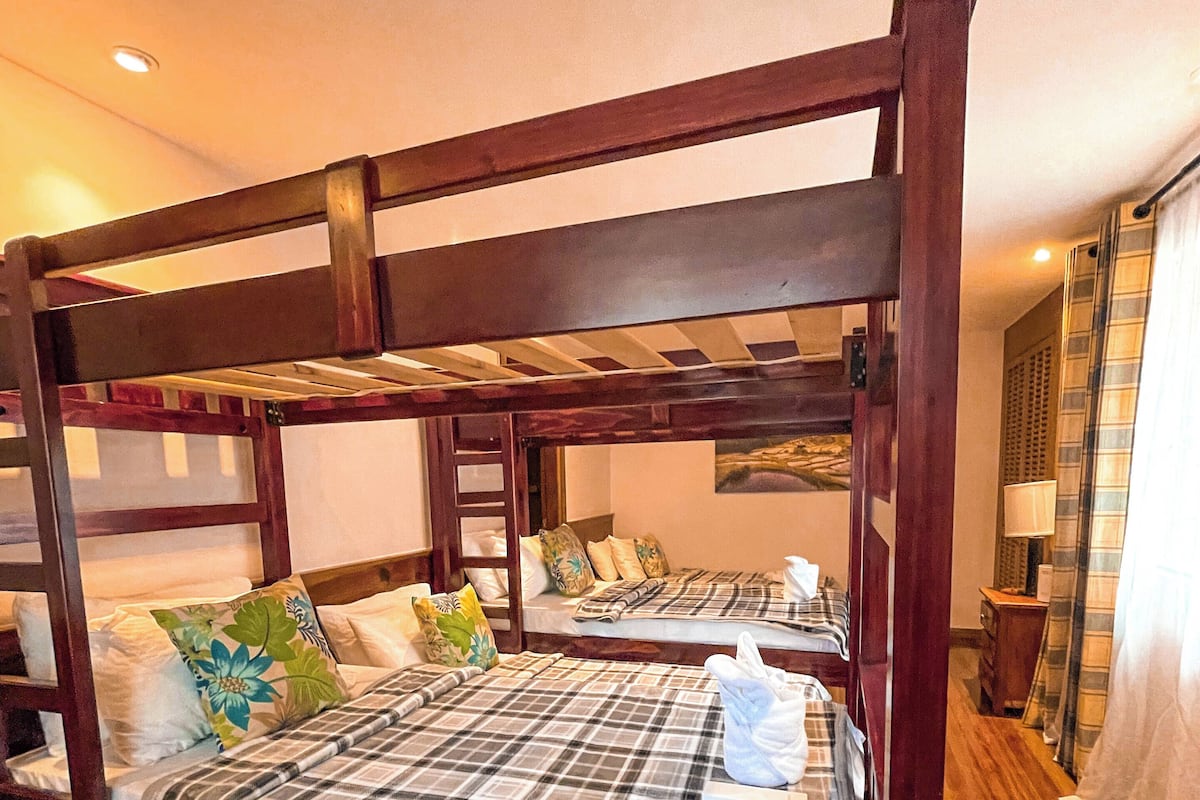 A bunk bed room with wooden frames, plaid bedding, and a wooden floor.