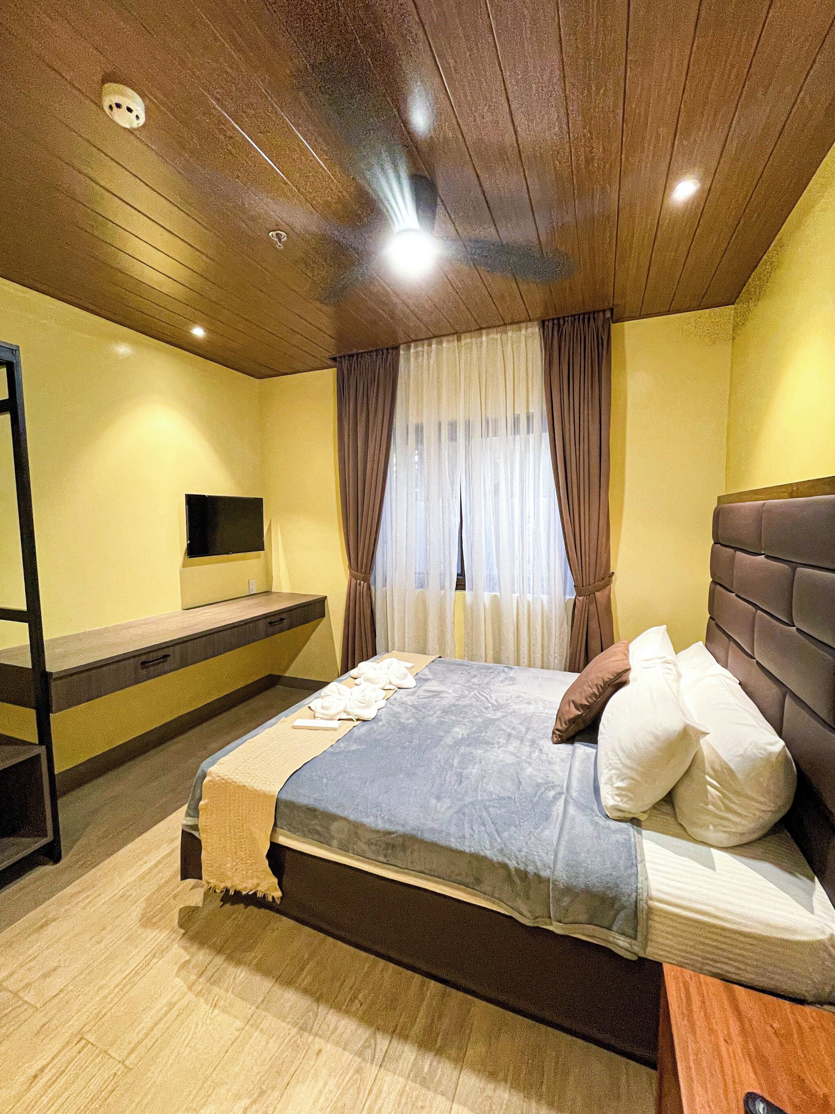 Un dormitorio con techo de madera, una cama con almohadas, una mesita de noche y un televisor montado en la pared.