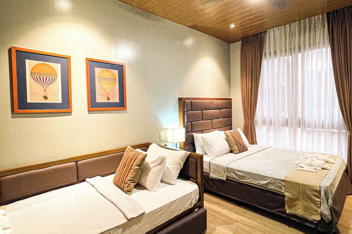 A hotel room with two beds, wooden ceiling, and framed artwork on the wall.