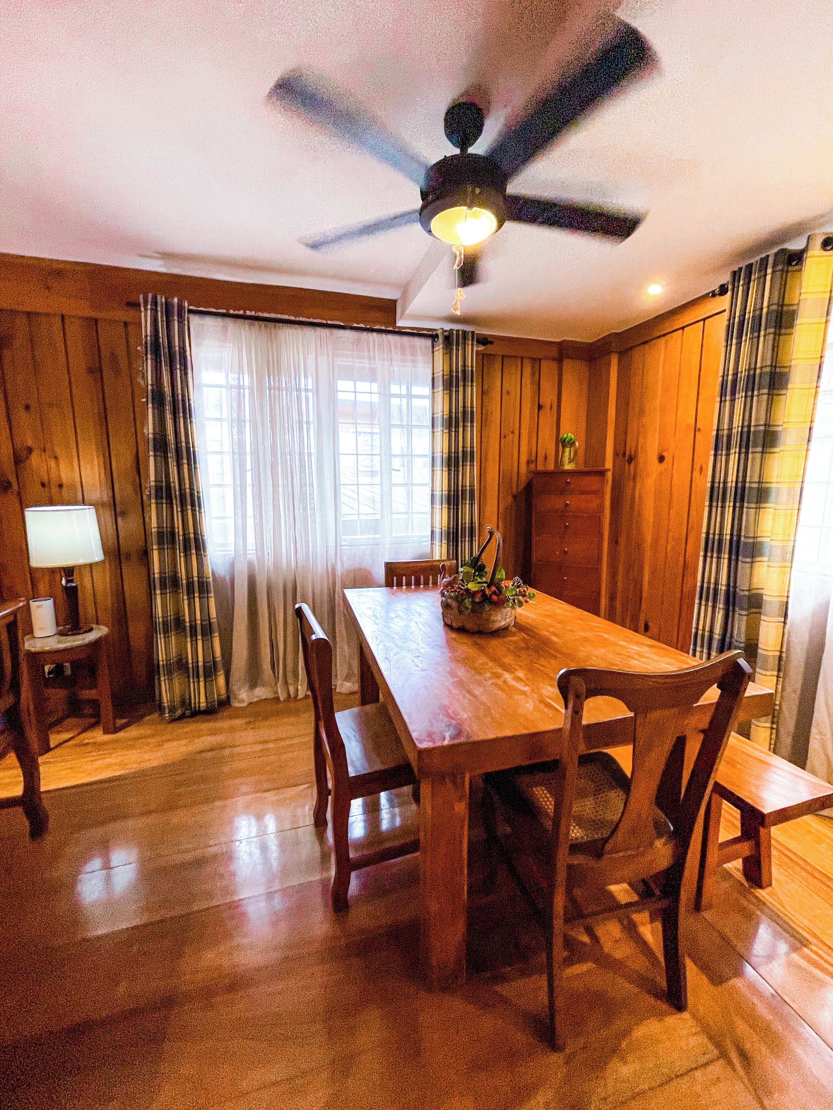 A dining area with a wooden table, chairs, a ceiling fan, and a lamp.