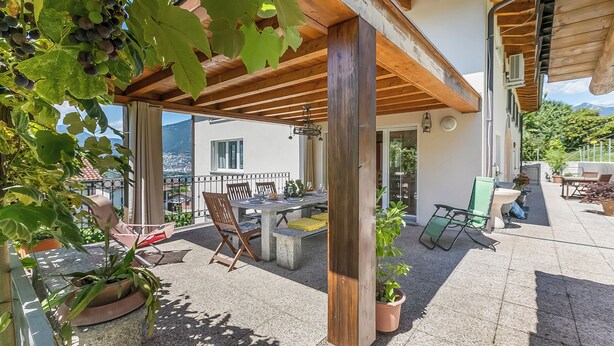 A covered patio with a table and chairs, potted plants, and a view of a mountain. - Gambarogno Vista Bella Apartments (Gambarogno)