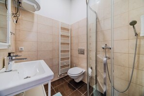 A bathroom with a white sink, a toilet, a glass shower enclosure, and a towel rack. - Old Town Heritage Suites (Osijek)