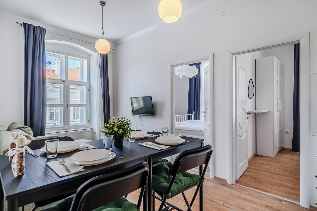 Un coin repas avec une table dressée pour deux personnes, une plante en pot et un téléviseur fixé au mur.