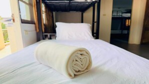 Ein ordentlich bezogenes Bett mit einem aufgerollten weißen Handtuch, im Hintergrund ein Etagenbett.