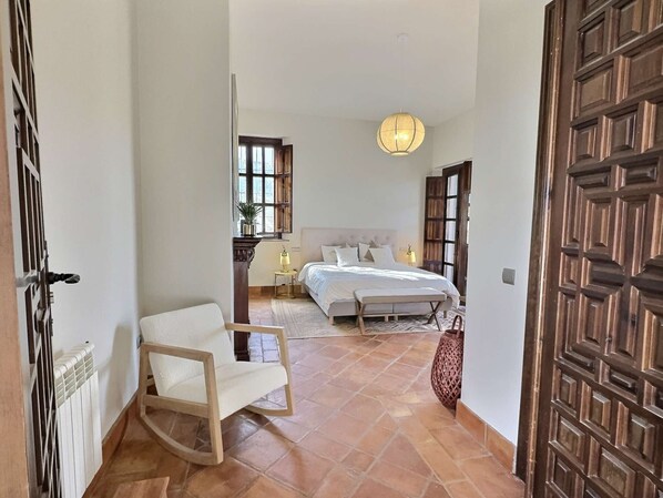 A bedroom with a bed, bedside tables, a hanging light fixture, and a view of a garden through a window. - Luxury Andalusian Escape | 11BR Villa w/ Pool, Jacuzzi & Stunning Views (Villanueva del Rosario)