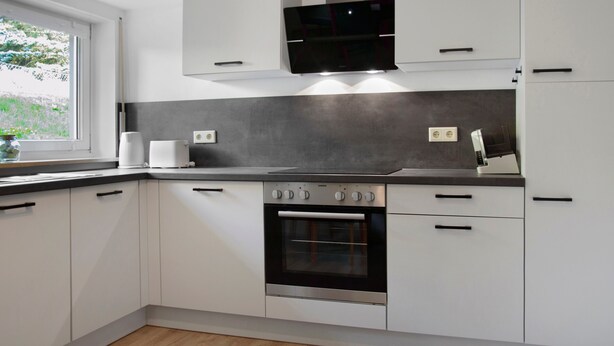 Una cocina moderna con armarios blancos, horno empotrado y microondas sobre la encimera.