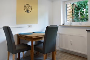 Et spiseområde med et træbord, to stole, et vindue med udsigt til grønne omgivelser og et skilt ophængt på væggen.
