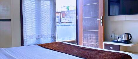 Habitación de hotel con cama, televisión, cafetera y ventana con vistas al exterior.