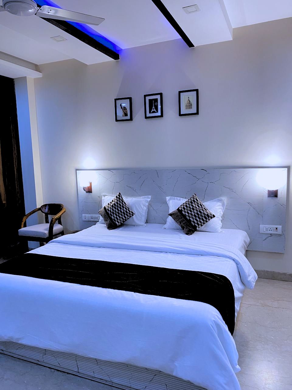 A modern bedroom with a large bed, a headboard with built-in lighting, and three framed pictures on the wall.