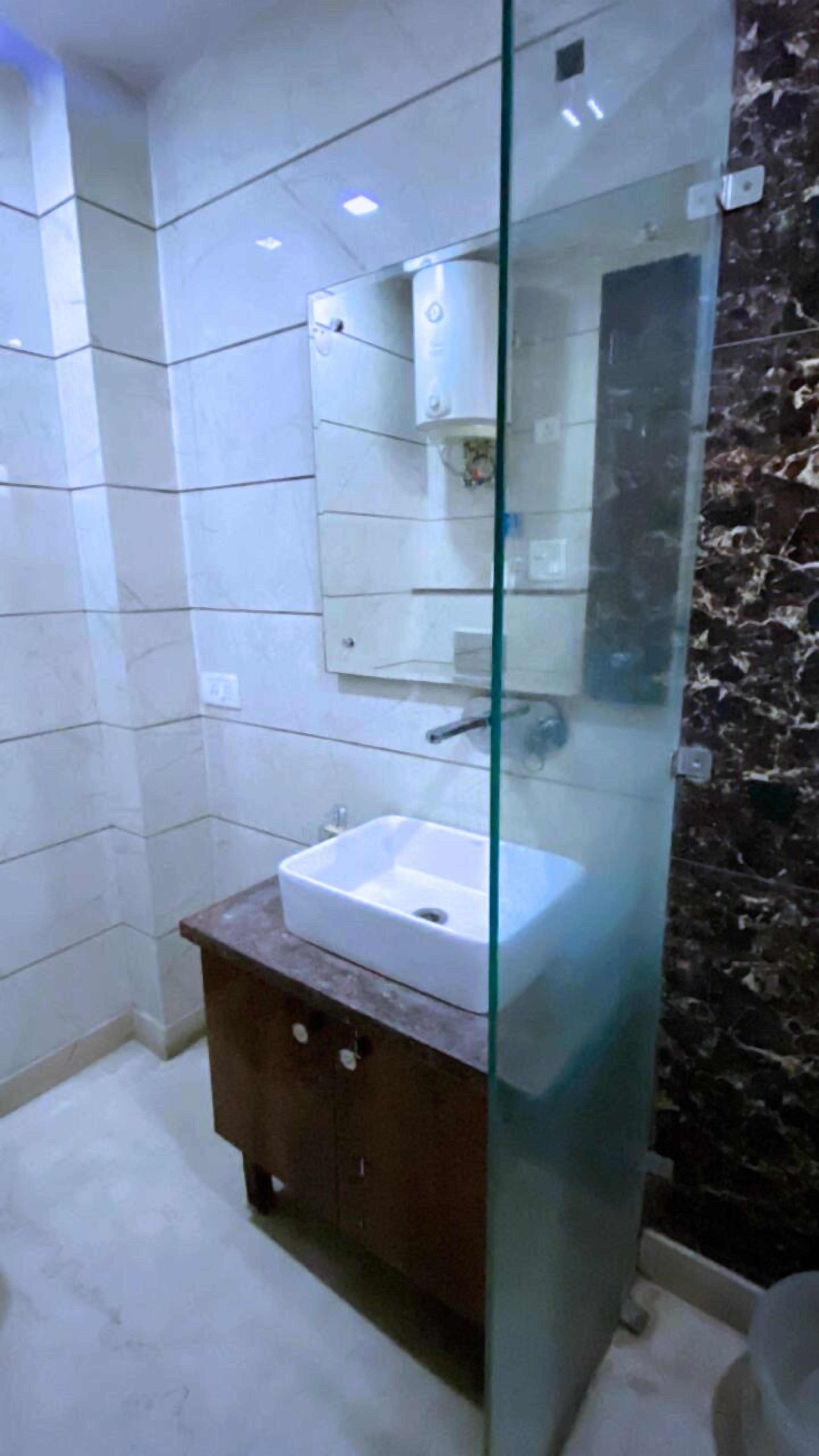 A modern bathroom with a glass shower enclosure, a white sink, and a marble-tiled wall.