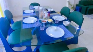 A dining area with a glass table, blue chairs, and a painting on the wall. - Cassava Stay (New Delhi)