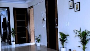 A spacious hallway with a polished marble floor, potted plants, and framed pictures on the walls. - Cassava Stay (New Delhi)