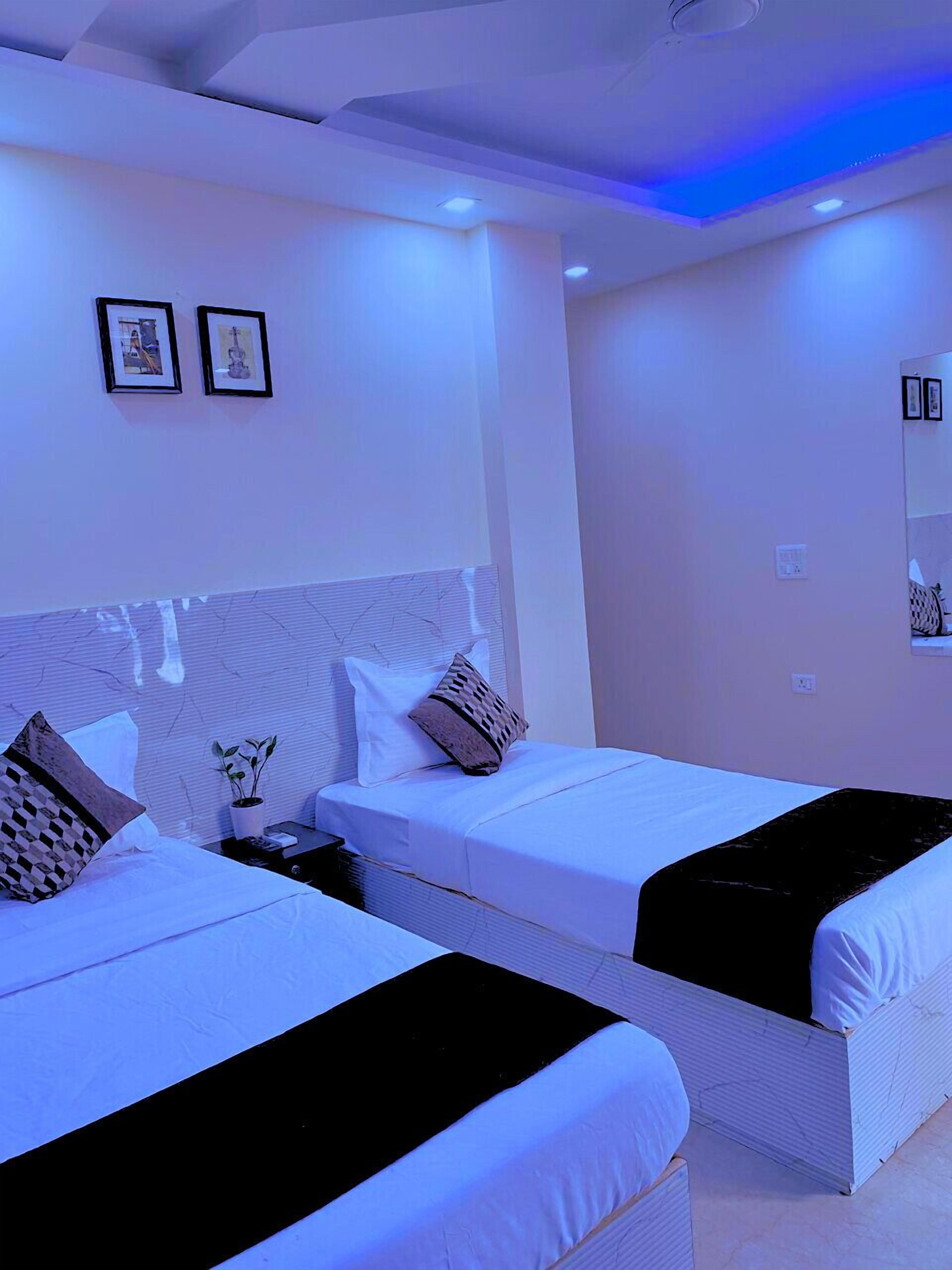 Habitación de hotel con dos camas, una mesita de noche, una planta en maceta y un televisor montado en la pared.