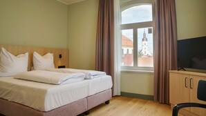 Habitación de hotel con cama, televisión, ventana con cortinas y vista a un edificio.