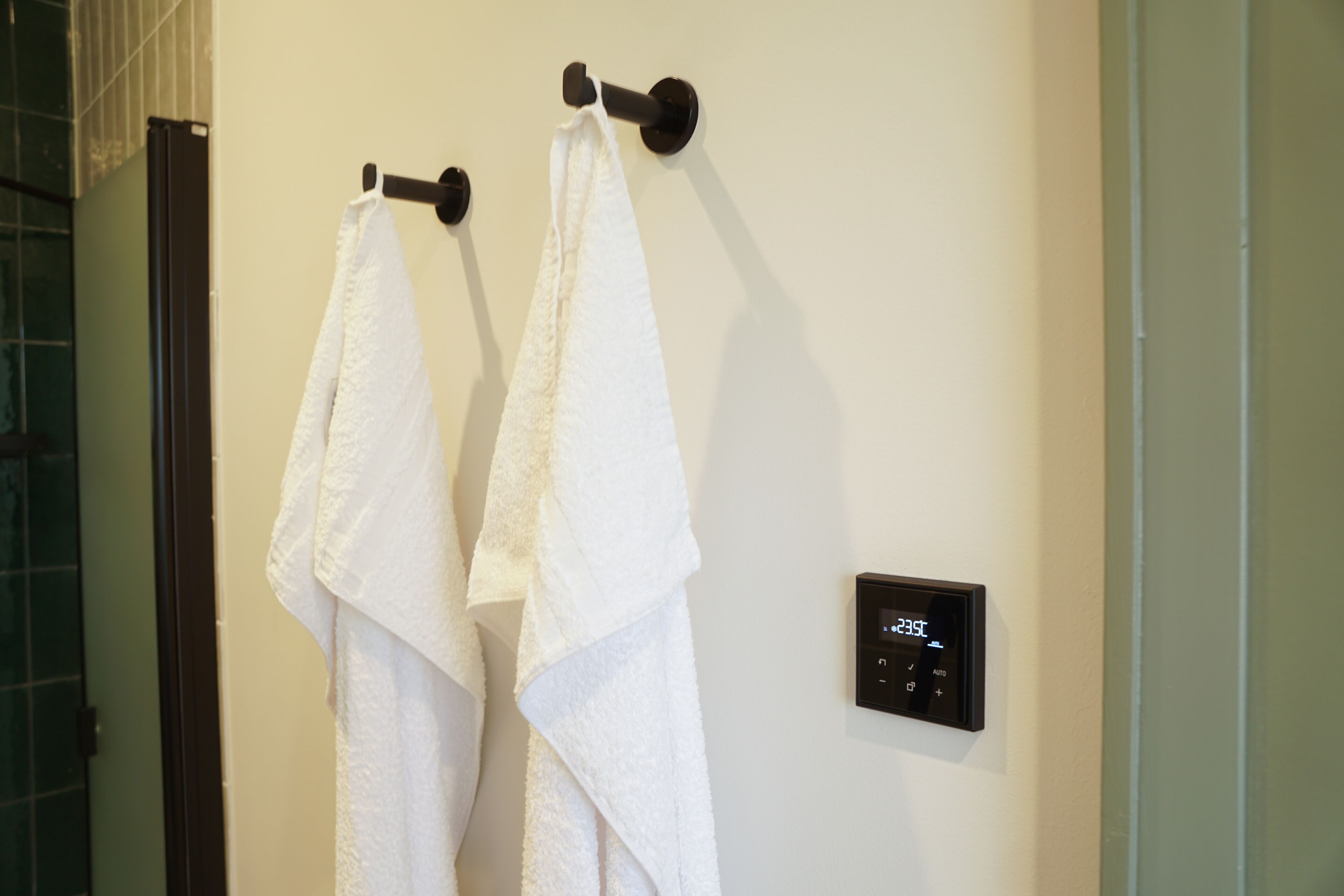 A bathroom with two white towels hanging on hooks, a digital thermostat, and a glass shower enclosure.