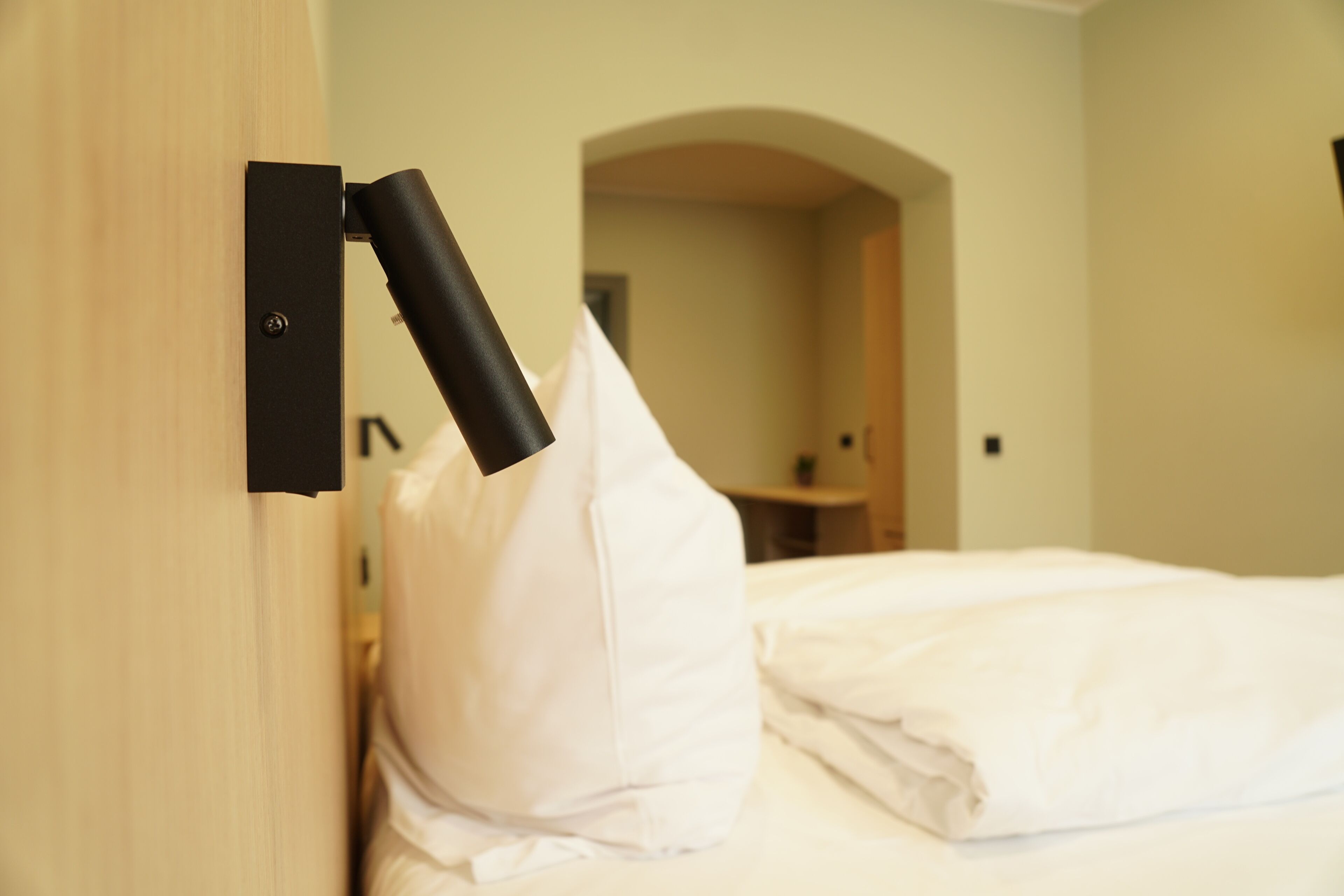 Een hotelkamer met een bed, een kussen, een wandlamp en een rondboogdeur.