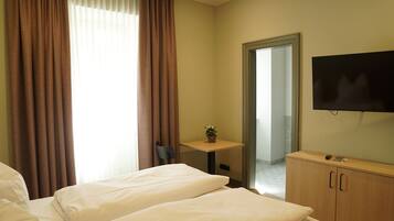 A hotel room with two beds, a TV, a small table with a plant, and a mirror.