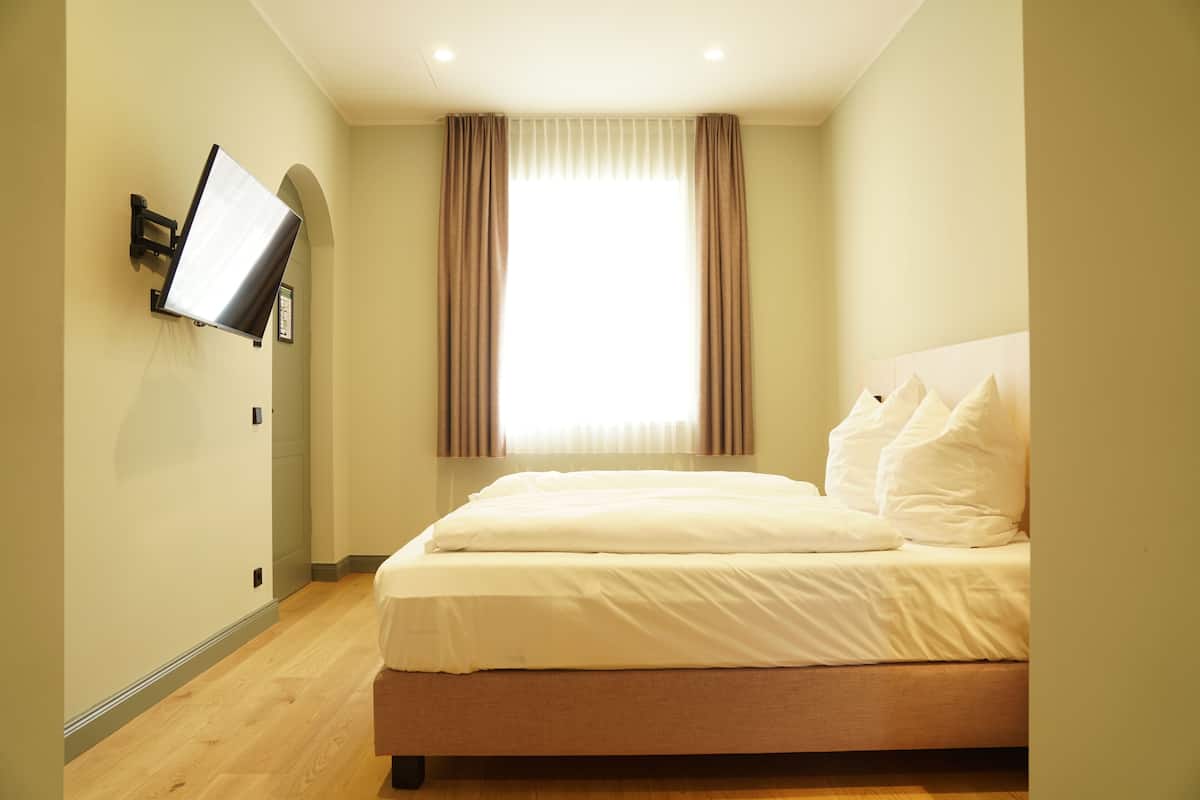 A bedroom with a bed, a television mounted on the wall, and a window with curtains.