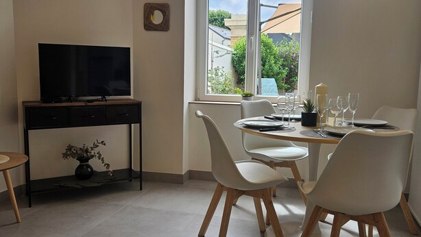 A dining area with a table set for four, a TV on a stand, and a window with a view of buildings and greenery. - Vineyard and Chateau Stay Vouvray (Vouvray)