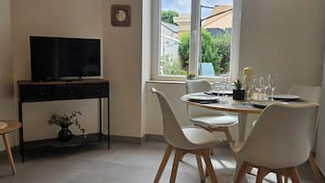 A dining area with a table set for four, a TV on a stand, and a window with a view of buildings and greenery.
